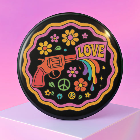 Round pinback button badge with a black background, featuring a retro illustration of a red revolver shooting out a rainbow flag that says “LOVE.” Surrounded by colorful 70s-style flowers and peace signs, outlined in wavy neon border. Glossy finish with vibrant pop colors and psychedelic design.