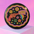 Round pinback button badge with a black background, featuring a retro illustration of a red revolver shooting out a rainbow flag that says “LOVE.” Surrounded by colorful 70s-style flowers and peace signs, outlined in wavy neon border. Glossy finish with vibrant pop colors and psychedelic design.