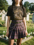 A black unisex crewneck graphic t-shirt featuring an ornate Victorian-inspired emblem printed on the chest in vintage gold and off-white. The centralized, symmetrical design showcases a classic coffin with a cross on the lid, flanked by wrought-iron cemetery gates. Beautiful scrollwork and decorative filigree flourishes surround the bold, retro serif text reading CEMETERY PICNIC SOCIETY. A crescent moon and stars sit at the top, completing this gothic memento mori graphic shirt.