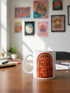 A glossy white porcelain ceramic mug featuring a vibrant maximalist design centered on the exterior. The artwork displays a retro 1970s-inspired rainbow arch composed of concentric bands in burnt orange, mustard yellow, and teal green. Inside the arch, stylized vintage bubble-serif typography in reddish-orange reads PEACE LOVE AND PLEASE DON'T TALK TO ME. The design evokes a groovy, hippie aesthetic mixed with sassy introvert humor.