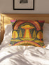 A colorful, patterned pillow with a whimsical design sits on a bed, featuring a rainbow, trees, and an alien-like figure.