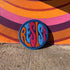 Round embroidered iron-on patch featuring "RESIST" text in bold flame design. Blue border surrounds navy background with orange, red, and blue flame-style lettering. 3x3 inch political activist patch with premium twill fabric construction, perfect for jackets, backpacks, and clothing customization. Anti-establishment protest accessory for resistance movements and political activism demonstrations.