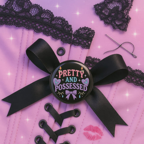 Glossy black pinback button featuring pastel-style text that reads “Pretty and Possessed” with a bow, candles, hearts, and sparkles.