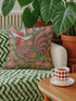 Square throw pillow cover with a printed faux embroidery design of a rooster wearing a white cowboy hat with red stars on a grass green background. The western chicken has a red comb and wattle, yellow beak and feet, and layered feathers in pink, green, orange, blue, and yellow with a rainbow striped tail. Pink and red flowers with yellow centers frame the bird. The stitched look is a flat 2D print on a smooth linen feel polyester cover with a hidden zipper, not raised embroidery.