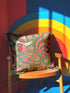 Square throw pillow cover with a printed faux embroidery design of a rooster wearing a white cowboy hat with red stars on a grass green background. The western chicken has a red comb and wattle, yellow beak and feet, and layered feathers in pink, green, orange, blue, and yellow with a rainbow striped tail. Pink and red flowers with yellow centers frame the bird. The stitched look is a flat 2D print on a smooth linen feel polyester cover with a hidden zipper, not raised embroidery.