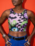 A close-up view of a sleeveless performance knit crop top featuring a vibrant pastel goth all-over print on a solid black background. The repeating pattern includes large black vampire bats flying over dripping, melted slime shapes in neon green. Wavy, warped checkerboard patterns in pastel pink, light purple, and black weave through the design. The graphic is finished with stylized, oversized pastel floral motifs and large open eyeballs staring outward.