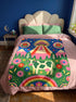 A rectangular velveteen minky blanket with a bright, maximalist design. The top half features a vibrant blue sky with a pink, green, and yellow UFO beaming rays down over hot pink snow-capped mountains. The bottom half shows a grassy green field with a white cow covered in dark spots, surrounded by large, colorful red, pink, and blue retro flowers, pine trees, and a rainbow arch at the very bottom. The reverse side is a fluffy off-white sherpa.