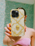A person is holding a phone with a skull design on the case, taking a selfie in front of a green wall.