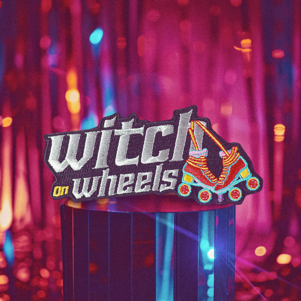 Embroidered patch featuring 'Witch on Wheels' text in metallic silver and white. Colorful roller skate design with vibrant rainbow hues. Fun, retro-inspired accessory for skaters and witchy enthusiasts. Ideal for jackets or bags.