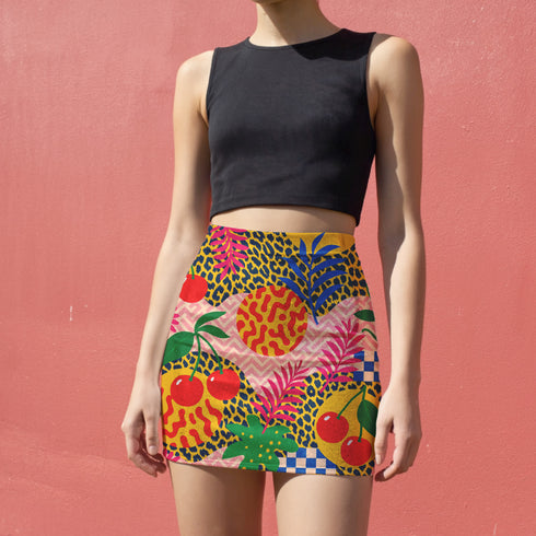 A woman wearing a black crop top and a colorful skirt with a pattern of fruits and flowers.