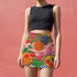 A woman wearing a black crop top and a colorful skirt with a pattern of fruits and flowers.