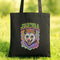 A black tote bag with a colorful graphic design featuring a cartoon-like creature with a flower crown and the text "THE FUTURE IS FEMME & FERAL" printed on it.