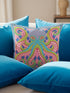 A square decorative throw pillow cover featuring a highly symmetrical bright octopus design. The octopus has a turquoise blue body with a diamond patterned head and eight curled tentacles detailed in bright pink and lime green. The background is a repeating diamond argyle pattern in royal blue and light pink. The artwork is a flat two dimensional print that mimics the textured look of intricate crewelwork embroidery. The pillow features a hidden zipper on the bottom edge. No insert included.