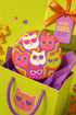 A close-up photograph of a glossy round ceramic coaster featuring a retro 70s psychedelic design. The artwork displays a cluster of six stylized cat face illustrations, each wearing a different pair of sunglasses including retro round and cat-eye shapes. The cats are colored in solid shades of white, hot pink, purple, and lime green. They are set against a vibrant background of wavy, swirling lines in bright orange, red, and purple. The top surface has a highly reflective clear glaze.