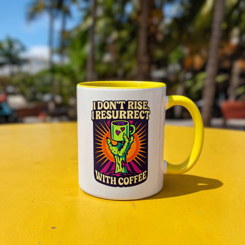 White ceramic coffee mug with red handle and interior, featuring a bold design of a zombie hand holding a coffee cup with the text “I Don’t Rise, I Resurrect With Coffee” in white and purple, accented with a neon green hand and orange sunburst background.