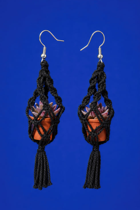 A pair of black earrings with orange pots and tassels hanging from the ends, set against a bright blue background.