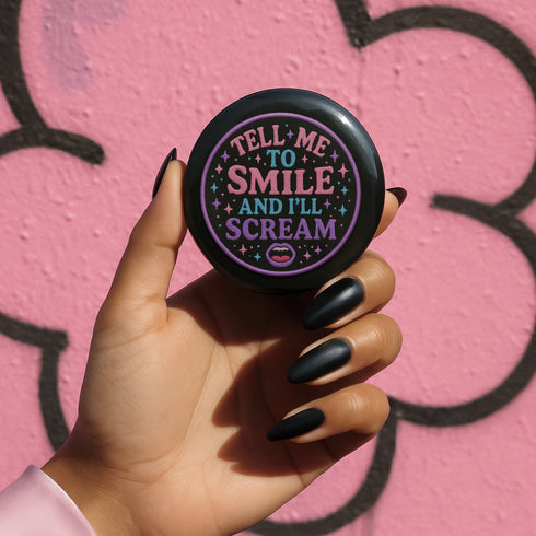 Glossy black pinback button with pastel-colored embroidered-style text that reads “Tell Me to Smile and I’ll Scream,” with lips icon and star accents.