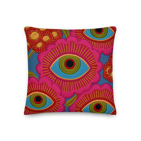 A square decorative throw pillow with a premium linen-feel texture. The design is a repeating pattern of stylized evil eyes on a dusty blue background. Each eye is rendered in turquoise, olive green, and black, and is framed by vibrant hot pink petals with radiating gold lines, resembling a flower or sunburst. The all-over print is colorful and has a visual texture that mimics embroidery. The pillow has a clean, knife-edge finish and a double-sided design, showcasing a bold, psychedelic pattern.