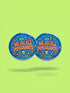A round 1.75 inch blue pinback button featuring retro psychedelic artwork. The text reads We Are All Immigrants in a groovy orange and red 1970s font style centered on the badge. A mystic third eye sits above the text while a small skull sits below it. Wavy rainbow lines in cyan, green, and orange radiate outward from the center along with small starbursts and lightning bolts. The button has a glossy finish reflecting light.