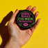 Glossy black pinback button featuring bold text 'Born to Make Cis Men Uncomfortable' in pink and green glitter fonts. Design includes melting skull outline and lips illustration. Button is round and 2.25 inches in diameter with a durable tinplate body and UV-resistant coating. Perfect for jackets, backpacks, or gifts for queer punks and feminists.