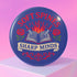 A round pinback button in blue with a glossy mylar face and metal construction. The design, in a traditional tattoo style, features a central open book with flames rising from its pages. Two silver swords with black hilts are crossed over the book. On either side of the book is a red rose with a green stem and leaves. Below the book is a cream-colored banner with the words "SHARP MINDS" in a black serif font. Above the book, the words "SOFT SPINES" are written in a curved, red font.