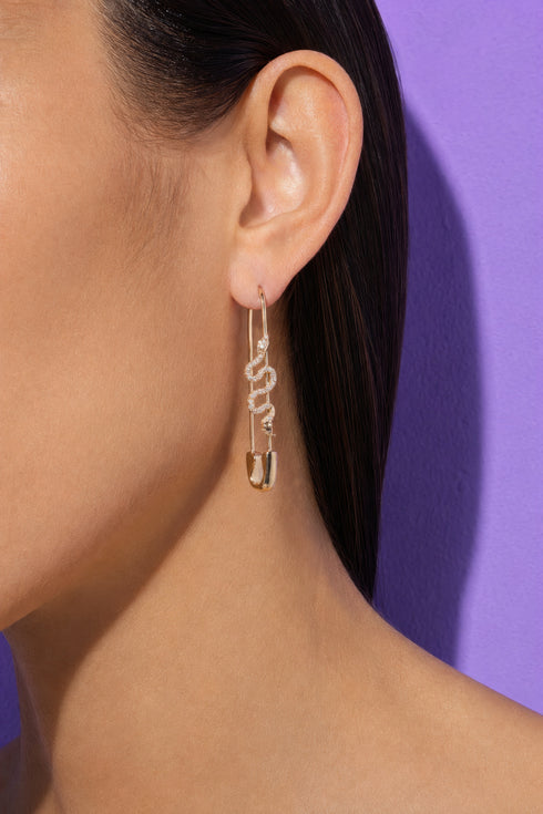 A close-up of a person's ear wearing a pair of gold earrings with a snake design.