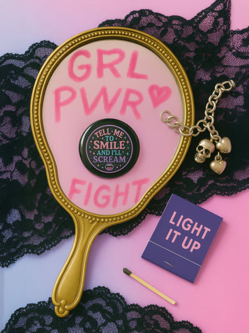 Glossy black pinback button with pastel-colored embroidered-style text that reads “Tell Me to Smile and I’ll Scream,” with lips icon and star accents.