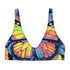 Butterfly-print bikini top with a vivid psychedelic monarch wing design in neon yellow, orange, and pink on a black base. Features a scoop neck, sports bra-style silhouette, and wide shoulder straps. Floating over a bright turquoise swimming pool, this swim top blends Y2K rave energy with bold festival fashion. Perfect for alt-girls, beach rebels, and dopamine dressers craving color-drenched swimwear.