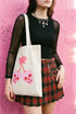 Black 15 x 16 inch 100% cotton tote bag with a kawaii pastel goth cherry-skull design printed on the front. The artwork features two soft pink skulls shaped like cherries, connected by red stems and topped with a bright pink bow. Cute, spooky, coquette, and alt-inspired everyday tote.