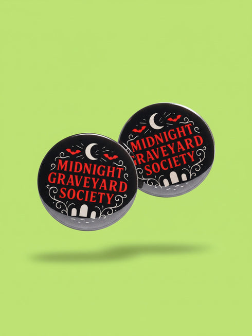 A collection of four glossy black circular pinback buttons featuring striking red and white gothic illustrations. One button shows "Midnight Graveyard Society" text with bats and tombstones. Another reads "Cemetery Picnic Society" with a coffin and umbrella icon. A third features a detailed white skull and red roses with "Memento Mori" text below. The final pin displays "Nocturnal Flower Society" surrounded by floral vines.