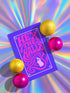 A vertical 5x7 greeting card made from premium 120lb silk cover stock with a slight sheen. The card has a deep purple background with a thin pink border. In the center, the words 'Hex the Halls' are written in a bubbly, psychedelic 70s-style font in shades of hot pink and light pink. Below the text is a stylized pink silhouette of a woman's face in profile with long, flowing, wavy hair. The design is reminiscent of retro witchcraft and groovy aesthetics, perfect for an alternative holiday.