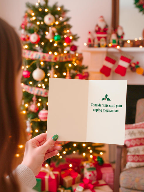 A 5x7 alternative holiday card with a white background and bold, punk-inspired typography. The text reads "Merry Crisis Happy New Fear" in dark green and red. The design features graphic elements like holly, stars, and safety pins, giving it a sarcastic, goth aesthetic. The inside message says "Consider this card your coping mechanism." This snarky, dark humor greeting card is perfect for a funny, unconventional Christmas, capturing a mental health humor and anti-capitalist vibe.