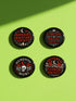 A collection of four glossy black circular pinback buttons featuring striking red and white gothic illustrations. One button shows "Midnight Graveyard Society" text with bats and tombstones. Another reads "Cemetery Picnic Society" with a coffin and umbrella icon. A third features a detailed white skull and red roses with "Memento Mori" text below. The final pin displays "Nocturnal Flower Society" surrounded by floral vines.