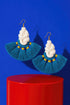 a pair of earrings with blue and white tassels, hanging from gold hooks against a blue background.
