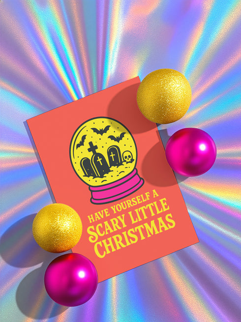 a Halloween-themed card with a spooky illustration of a cemetery and bats, surrounded by glittery gold and pink balls, with the text "Have Yourself a Scary Little Christmas" displayed on the card.