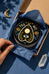 A close-up photograph of a glossy ceramic coaster featuring a Planchette occult design on a deep black background. The symmetrical graphic displays a central blue All-Seeing Eye with gold sunburst lines, topped by a white circle, and flanked by gold flowers with blue stems. At the top, the text "YES" is printed in gold on the left and "NO" on the right. Gold stars and crescent moons are scattered around the perimeter. The flat, round coaster has a highly visible high-gloss glaze.
