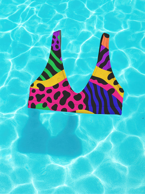 Colorblock animal print bikini top with neon pink, orange, green, purple, and blue abstract pattern. Scoop neck cut with wide straps, removable padding, double-layered fabric, UPF 50+, and made from soft, stretchy recycled polyester-spandex blend.