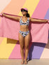 A two piece recycled high waisted swimsuit with a pastel goth checkered print in light lavender purple, pale mint green, and white squares with black cow print spots. The design features small black hearts and silhouetted bats with outspread wings printed throughout. The athletic style crop top has a deep scoop neck and matching thick straps, while the double layered bottoms have a supportive high waistband and cheeky cut with a solid black inner lining.