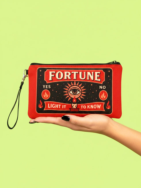 A rectangular red zippered pouch featuring a vintage-style tarot card design. The front displays the word FORTUNE in large beige capital letters. A central illustration shows a mystic eye emitting rays of light above a lit candle flame. The text YES and NO appears on the sides. A banner at the bottom reads LIGHT IT TO KNOW. The bag is crafted from red polyester with a linen-like woven texture, featuring a black zipper and a removable black nylon wrist strap. The interior is white.