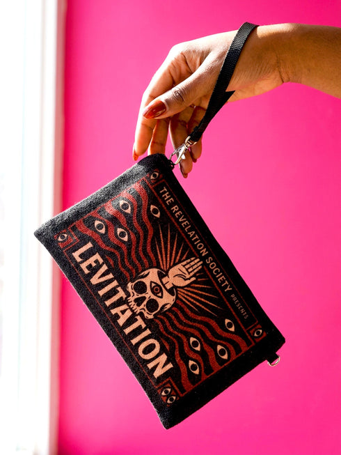 A rectangular makeup bag featuring a vibrant psychedelic print with gothic elements. The fabric texture is clearly visible showing a woven linen-like polyester grain. A black zipper runs across the top edge with a black detachable nylon wrist strap clip on the side, showcasing the approximately nine by six inch dimensions. The print includes high contrast neon colors and trippy swirling patterns typical of maximalist decor.
