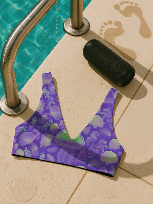 Bralette-style bikini top featuring a high neckline and vibrant jellyfish print in iridescent purples, blues, and greens on a lilac background. Made of recycled polyester and LYCRA XTRALIFE, this double-layered swim top includes removable padding, UPF 50+ protection, and is available in sizes XS to 3XL. Great for raves, beach days, and summer festivals.