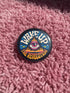 A round pinback button featuring a retro psychedelic design. The central focus is a stylized Eye of Providence in a pink triangle, surrounded by vibrant orange and yellow flames. Behind the triangle are teal and petrol blue sunburst rays. The text "WAKE UP" curves across the top in cream wavy letters, and "THE REVOLUTION" curves along the bottom in orange. The button has a glossy finish and is available in 1.75 inch or 2.25 inch sizes.