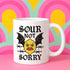 White ceramic 11oz coffee mug featuring a bold tattoo-style graphic with an angry yellow lemon face, black bat wings, and barbed wire details. The design reads “SOUR NOT SORRY” in gothic black lettering above and below the lemon. C-handle, durable construction, dishwasher and microwave safe. Graphic is high-contrast and punk-inspired, perfect for adding attitude to your drinkware collection.