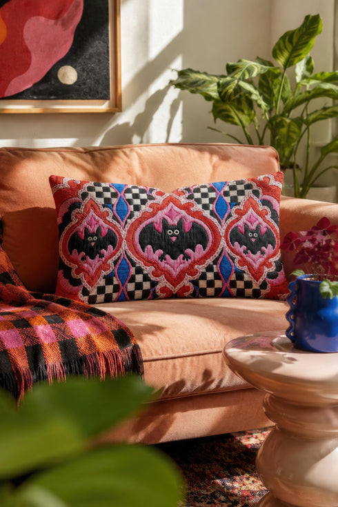 Rectangular 20x12 inch lumbar pillow cover in red featuring printed faux embroidery of three black bats with white eyes and pink noses, each framed in an ornate ogee medallion with pink flame stitch centers, black and white checkerboard accents, and cobalt blue diamonds. Whimsigoth damask bat design printed on both sides with a hidden zipper, crafted from soft linen look polyester for spooky maximalist home decor.