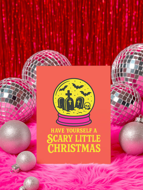 a card with a Halloween-themed illustration, surrounded by disco balls and ornaments on a pink surface.