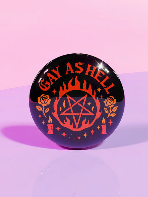 Round glossy pinback button measuring 2.25 inches with bold red graphic design on a black background. Text reads “Gay As Hell” above a red pentagram surrounded by flames, stars, roses, and candles. Made of tinplate with a safety pin back and a scratch-resistant mylar finish. The button features a high-gloss surface and is lightweight and durable, perfect for jackets, bags, or accessories.