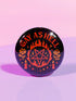 Round glossy pinback button measuring 2.25 inches with bold red graphic design on a black background. Text reads “Gay As Hell” above a red pentagram surrounded by flames, stars, roses, and candles. Made of tinplate with a safety pin back and a scratch-resistant mylar finish. The button features a high-gloss surface and is lightweight and durable, perfect for jackets, bags, or accessories.