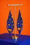 A pair of blue and gold beaded earrings with long, dangling designs, displayed on a gold stand against an orange background.
