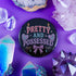 Glossy black pinback button featuring pastel-style text that reads “Pretty and Possessed” with a bow, candles, hearts, and sparkles.