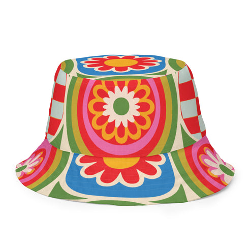 Reversible all-over print unisex bucket hat featuring two distinct bold designs. Side one showcases a psychedelic wavy stripe pattern in deep red, orange, green, blue, cream, and blush. Side two features a retro 70s groovy floral medallion print with large daisy motifs, red petals, yellow centers, and concentric pink, orange, and green rings on a cream background. Made from 100% polyester with a soft linen-feel texture. Moisture-wicking and breathable. Unisex sizing: XS/S and M/L/XL.